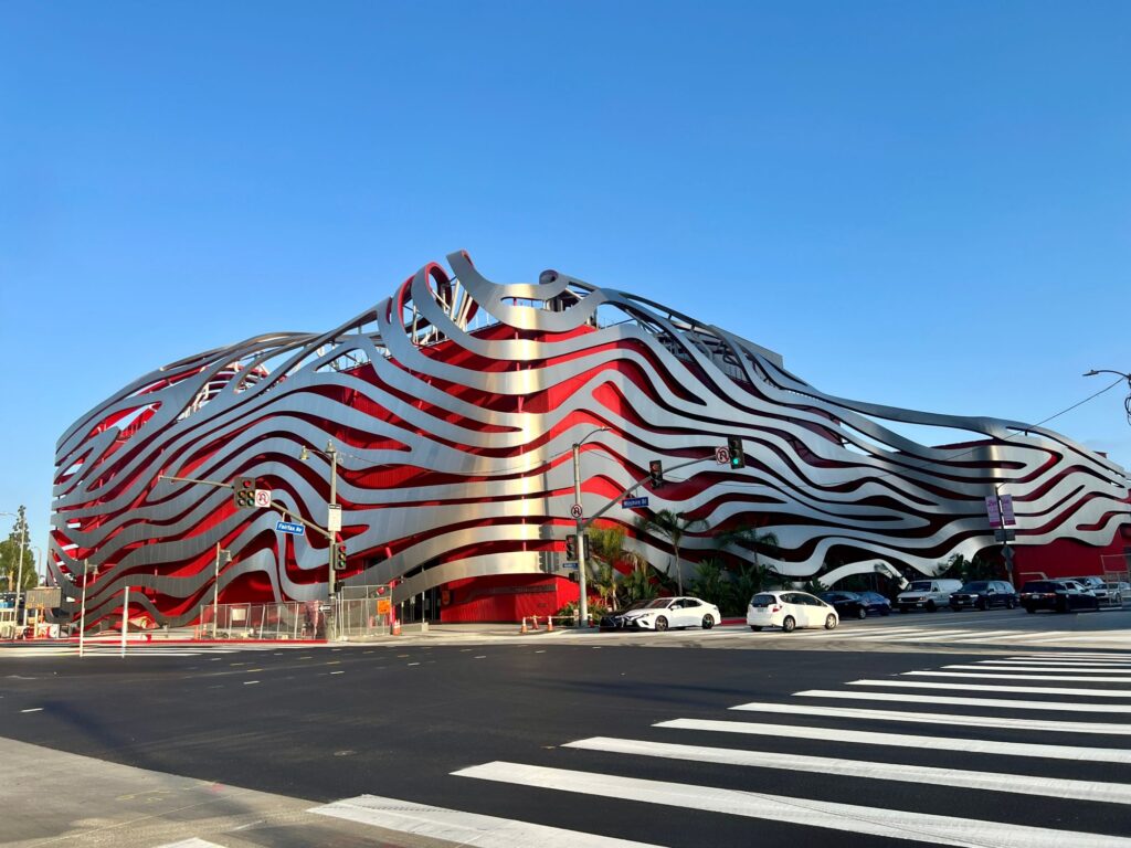 Striking curved building facade of Petersen Automotive Museum with flowing red and silver striped pattern, resembling ribbons or waves, clear blue sky above by Vesperstock.